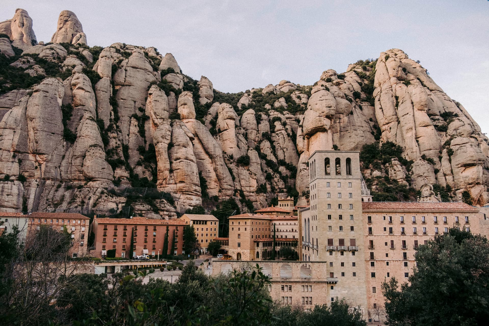 a large building with a large rock formation behind it with Montserrat in the background